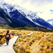 Woman walking on boardwalk across field near mountains
