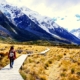 Woman walking on boardwalk across field near mountains